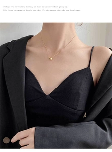 Close-up of minimalist gold ball pendant necklace worn by a model in elegant attire