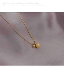 Detail of gold snake chain necklace featuring polished and frosted double ball pendants
