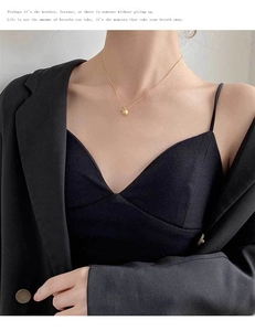 Close-up of a minimalist matte gold ball pendant necklace worn on a female model