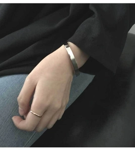 Close-up of a silver-toned flat steel cuff bracelet and thin ring worn on wrist