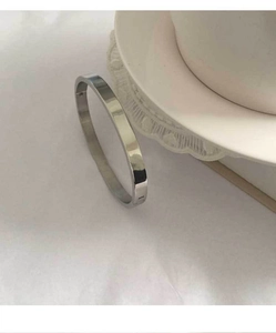 Detailed view of a polished silver stainless steel bangle leaning on white ceramic