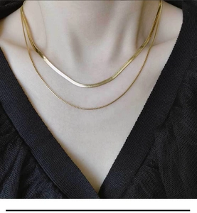 Détail d'un collier à double chaîne serpent dorée sur un fond de dentelle noire