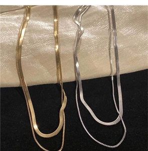 Détails de colliers double rang en maille serpent dorés et argentés sur tissu doux