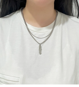 Detailed shot of a layered silver feather pendant necklace on a simple white t-shirt
