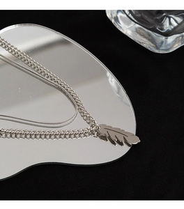 Detail of silver feather pendant with layered curb and snake chains on a mirror surface