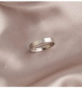 Nahaufnahme eines polierten flachen Edelstahlrings auf rosa Satin-Stoffhintergrund