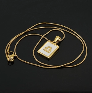 Macro shot of 18K gold plated Libra pendant with white enamel on rectangular plate
