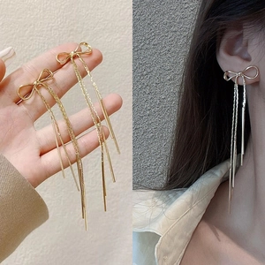Détail de boucles d'oreilles longues à pampilles avec nœud en or et argent sur modèle