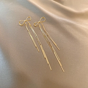 Détail macro de boucles d'oreilles à pompons dorés avec un nœud papillon sur soie
