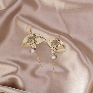 Macro detail of golden folding fan earrings with dragon carving and pearl tassels