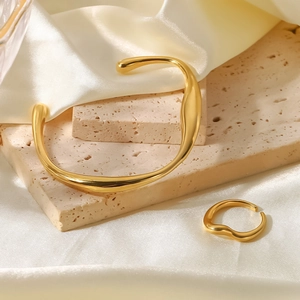 Poliertes Goldarmband und Ring im Flüssigkeits-Stil auf edlem Seidenhintergrund
