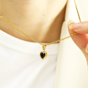Macro detail of gold heart necklace featuring a black zircon stone on model collarbone