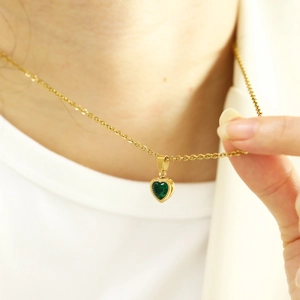 Close-up of golden necklace featuring an emerald green heart zircon pendant on neck