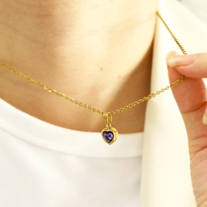 Detail of gold heart pendant necklace featuring a purple zircon and milgrain edges