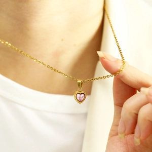 Close-up of a pink heart-shaped zircon necklace with gold beaded bezel on a female model