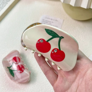 Elegant cherry acetate hair claw clip with rhinestones shown in a lifestyle hand-held view