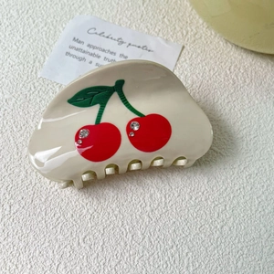 Close-up of cream acetate hair claw clip featuring red cherry patterns and sparkling rhinestones