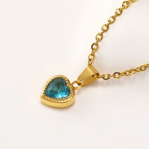Macro shot of gold heart pendant necklace featuring blue zircon and beaded metal edges