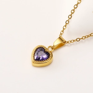 Macro shot of gold heart pendant featuring a faceted purple zircon and beaded metal edges