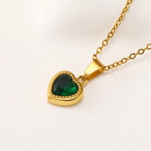 Close-up of heart-shaped gold necklace with emerald green zircon and beaded detailing