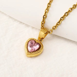 Macro detail of a gold heart pendant with pink zircon and milgrain edge on a fine chain