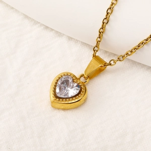 Macro shot of gold heart pendant with heart-cut clear zircon on white linen