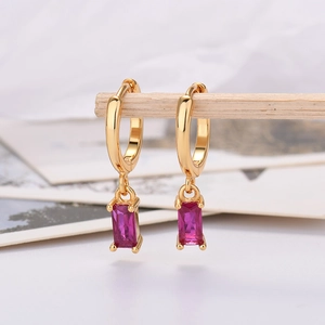 Macro detail of gold earrings with rectangular rose red zircon stones on wood stand