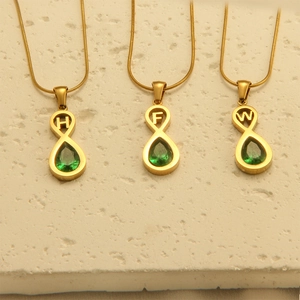Detailed shot of golden alphabet necklaces H, F, W with green teardrop gemstones