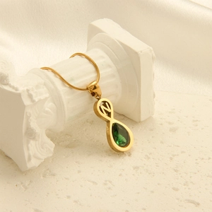 Detail of gold letter N necklace featuring a teardrop green gemstone on a marble column