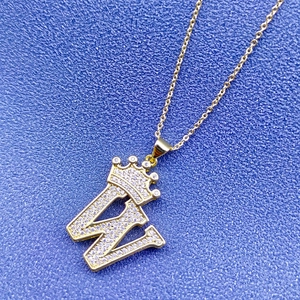 Détail du pendentif lettre W dorée avec couronne sertie de zircons sur fond bleu