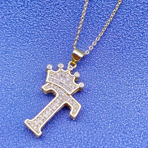 Vue détaillée du pendentif couronne lettre T en or 18k serti de strass sur fond bleu