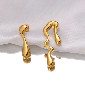 Gros plan de boucles d'oreilles asymétriques en or aux formes fluides sur soie blanche