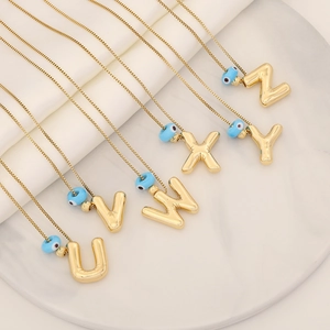 Colliers pendentifs alphabet dorés 18 carats avec perles œil bleu sur fond de marbre