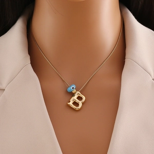 Gros plan d'un collier doré avec perle œil bleu et pendentif lettre B sur modèle