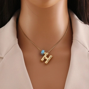 Détail du pendentif lettre H en or 18k avec charm œil bleu sur une chaîne fine