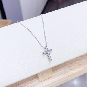Macro detail of silver cross necklace with pavé-set zircons on white leather stand