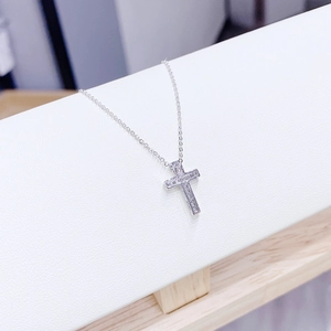 Macro shot of silver cross pendant with sparkling zircons on white leather texture