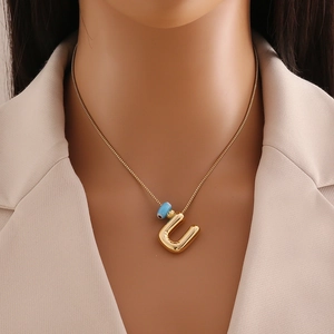 Détail d'un collier en or 18 carats avec pendentif lettre U et œil bleu sur mannequin