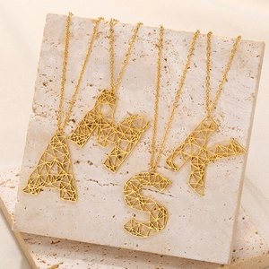 Detail van holle geometrische gouden letterhangers A M S K op een stenen bord