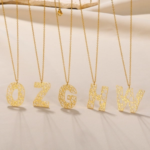 Detailweergave van gouden kettingen met holle geometrische letters O Z G H W op textiel