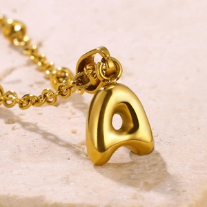 Polished 18K gold plated stainless steel 3D bubble letter A pendant necklace on stone background