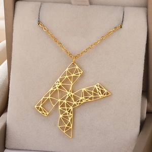 Macro-opname van gouden geometrische letter K-hanger in een beige luxe sieradendoosje