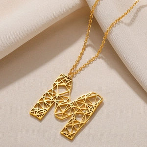 Gedetailleerde close-up van gouden M-letter hanger ketting met geometrisch rasterpatroon
