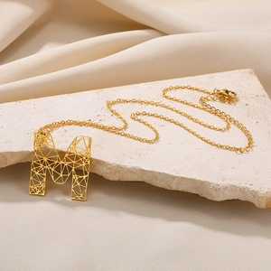 Detail van een vergulde halsketting met een geometrische holle letter M hanger op steen