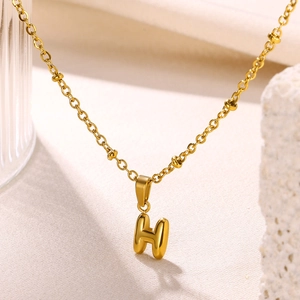 Macro detail of 3D bubble letter H pendant on a beaded gold stainless steel chain