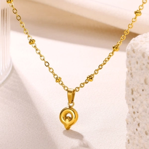 Detail of 18K gold-plated bubble letter pendant with station bead chain on white stone