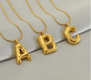 Golden 3D balloon letter A B C necklaces with sleek snake chains on grey silk background
