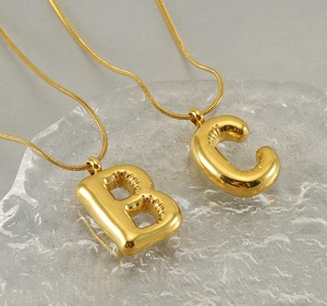 Close-up of golden balloon style letter B and C pendants on sleek snake chains