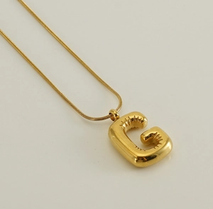 Macro shot of bubble letter G pendant with glossy gold snake chain on soft background