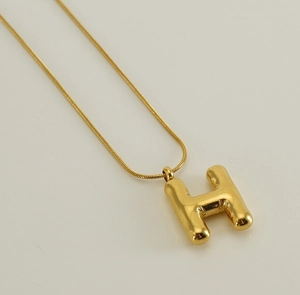 Macro detail of golden 3D bubble letter H pendant on a sleek snake chain necklace